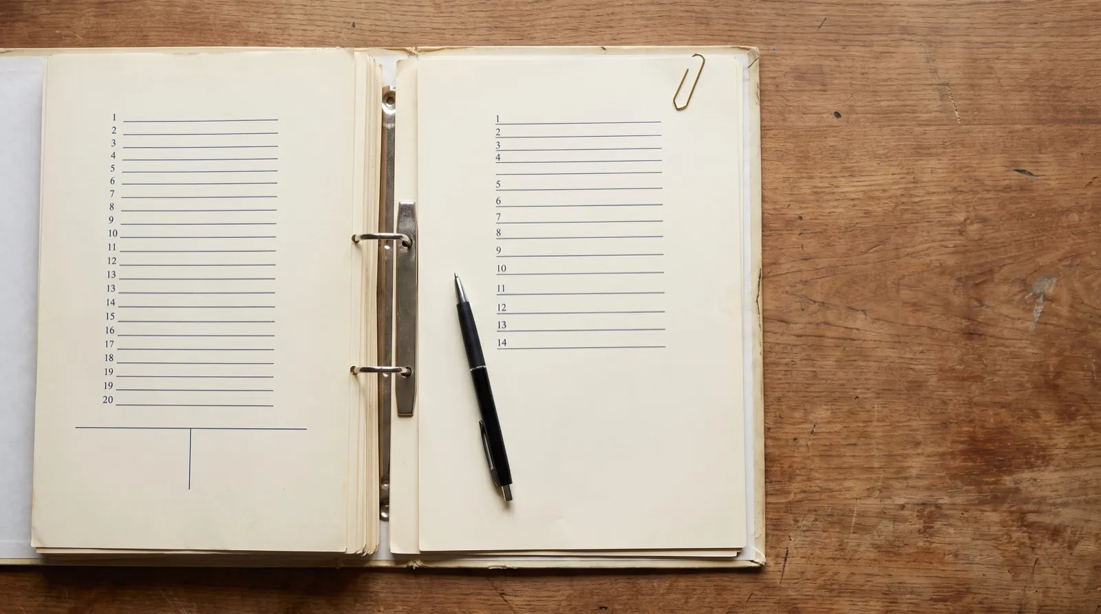 An open ring binder on a wooden desk, its two facing worksheet pages ruled with differently spaced numbered rows
