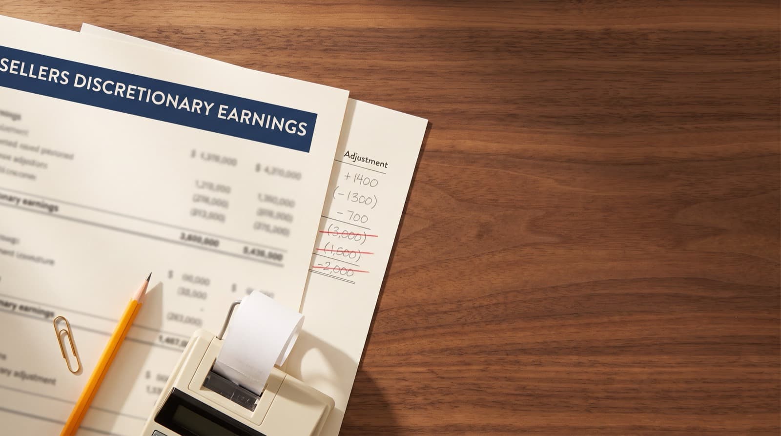 A business buyer comparing a broker listing packet against tax returns and a recast worksheet at a desk