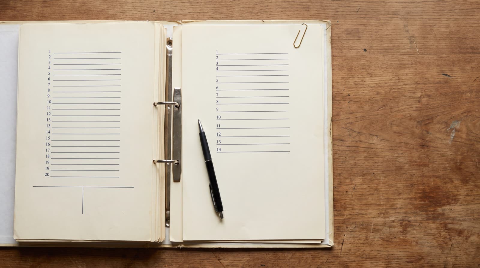 An open ring binder on a wooden desk, its two facing worksheet pages ruled with differently spaced numbered rows