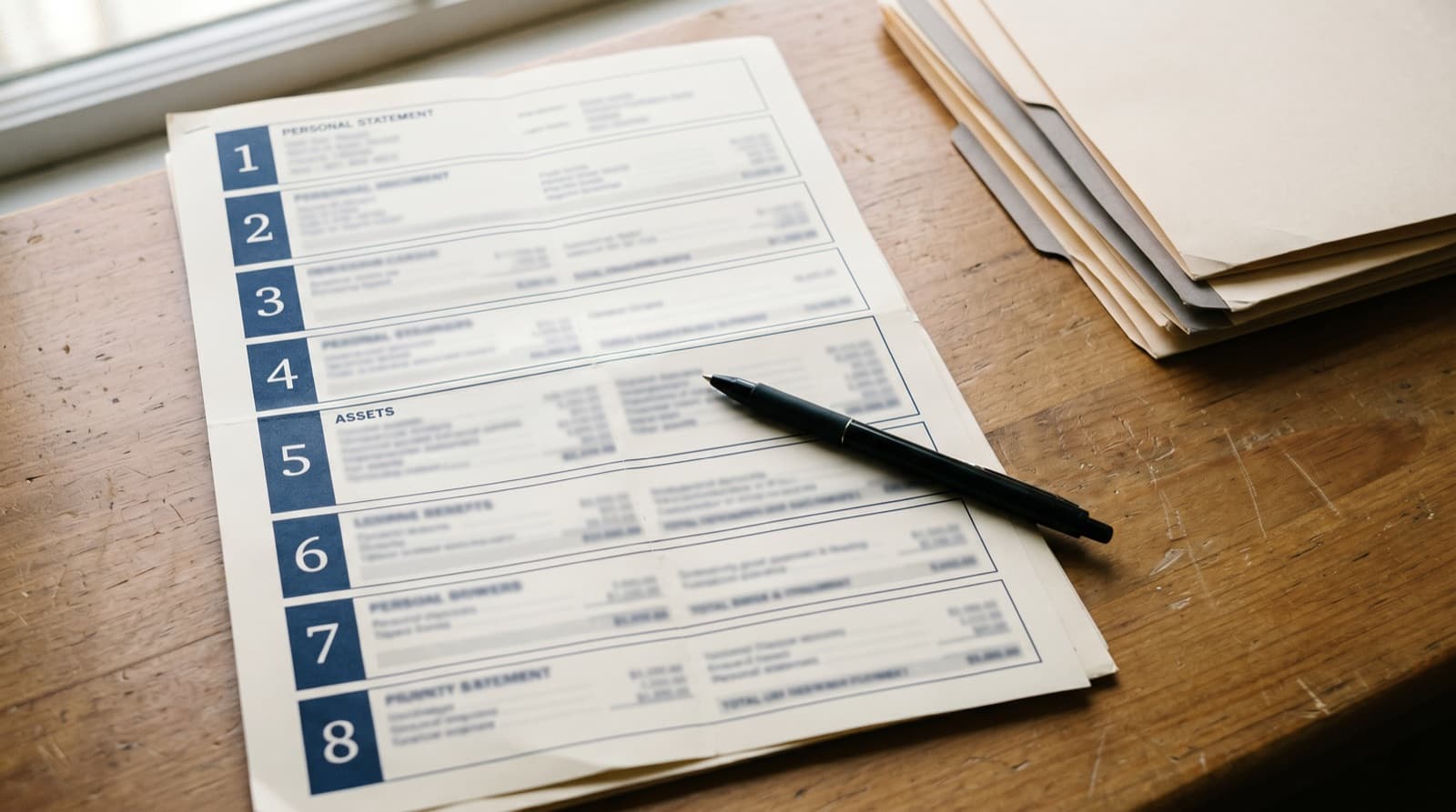 An SBA Form 413 personal financial statement on a clean desk with section dividers visible along the left margin and a black pen resting over Section 5
