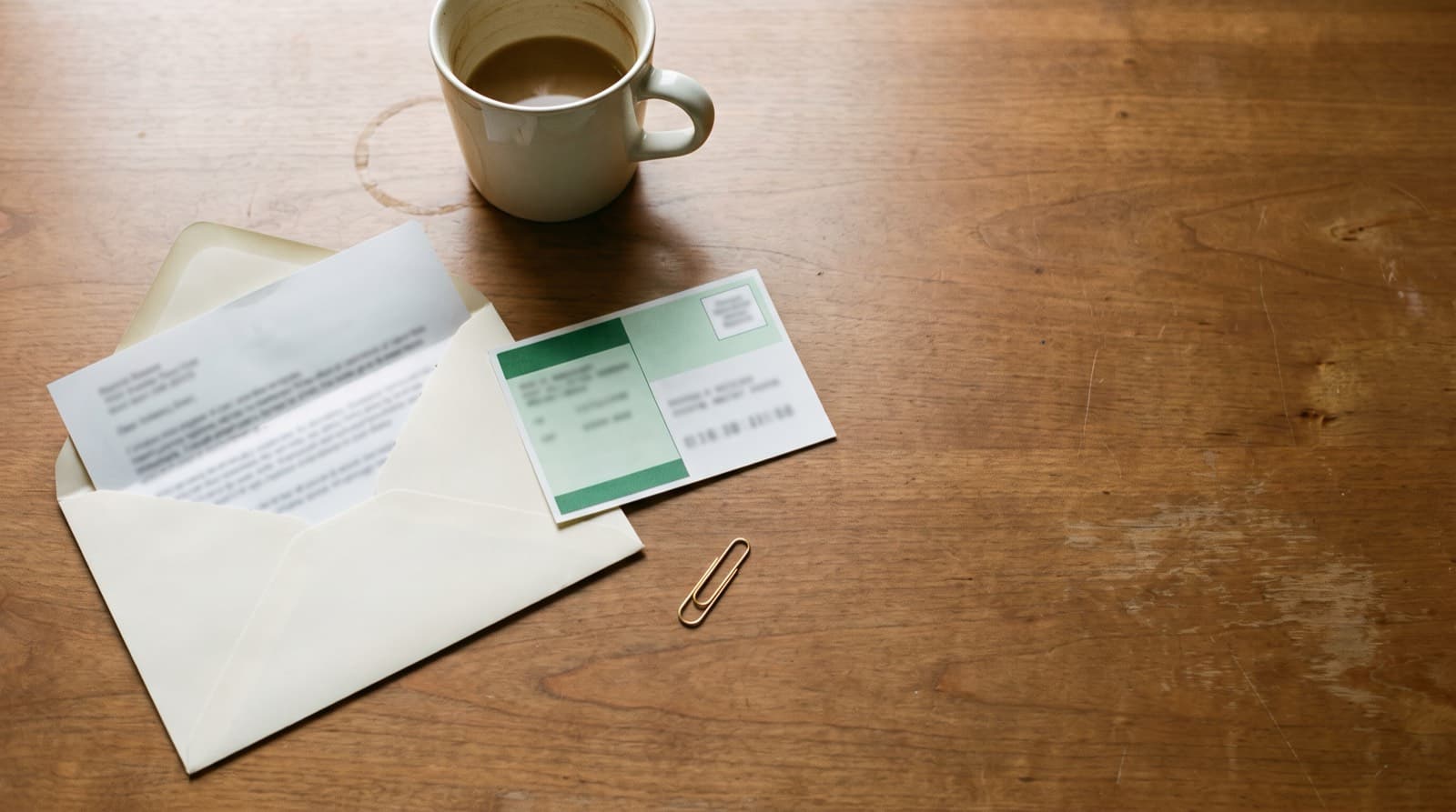 An opened envelope with a folded notice letter and a certified mail receipt card on a wooden desk beside a coffee cup